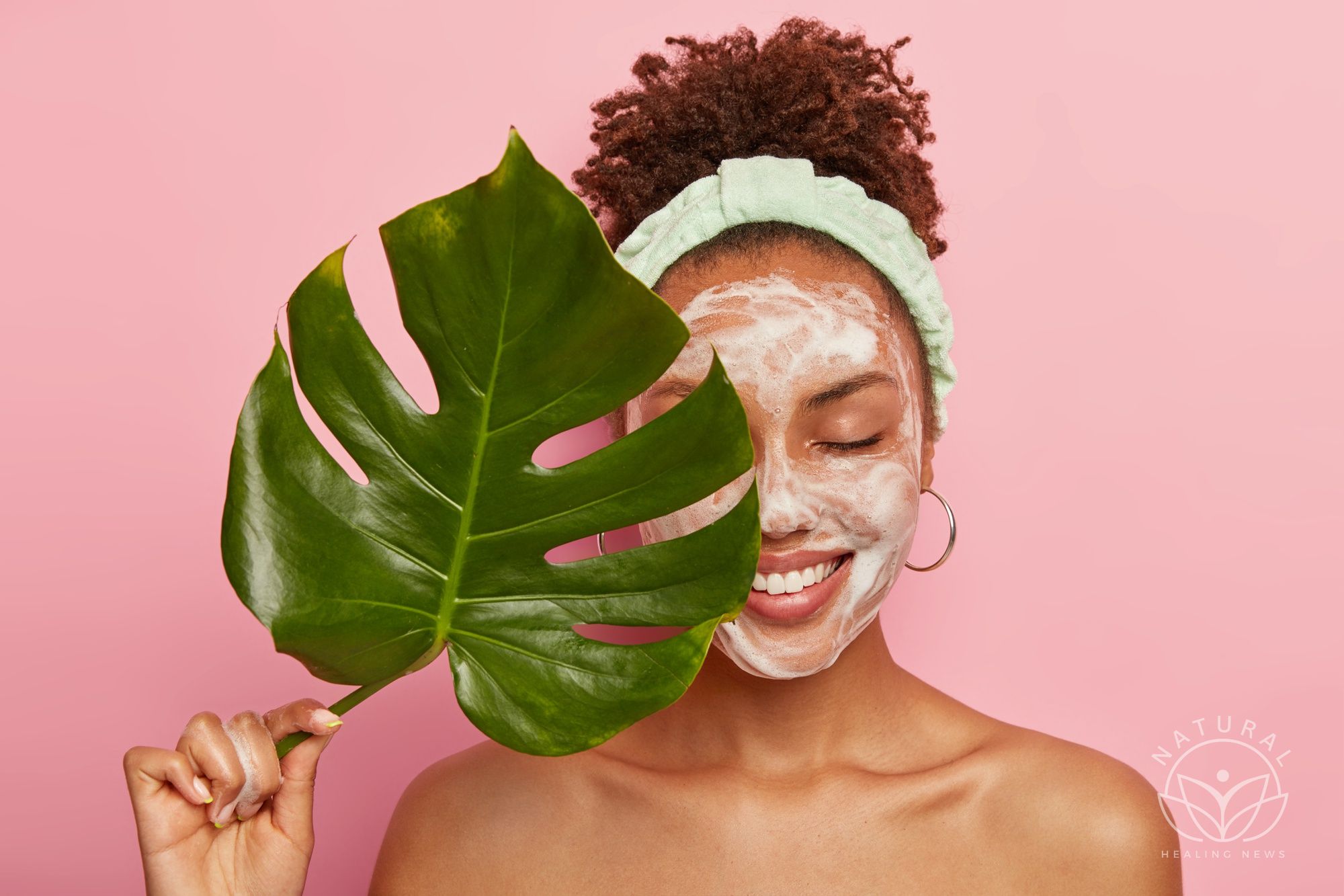 Free photo portrait of happy african american woman covers half of face with green leaf, cleans face, washes with bubble soap, stands topless, cares aboout her beauty and body